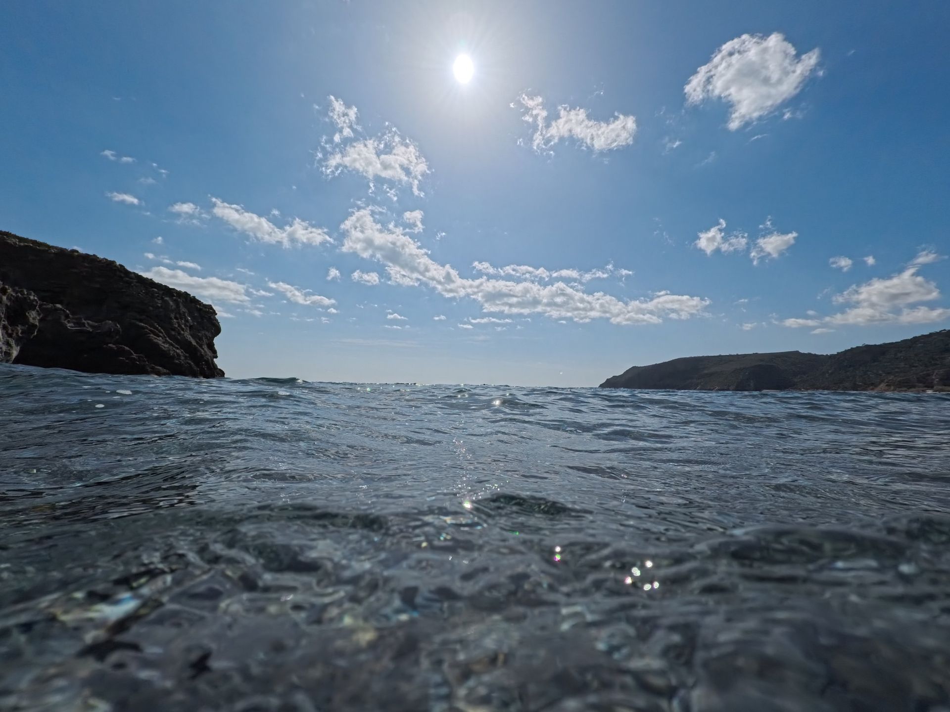 Sun high over the sea under a clear blue sky