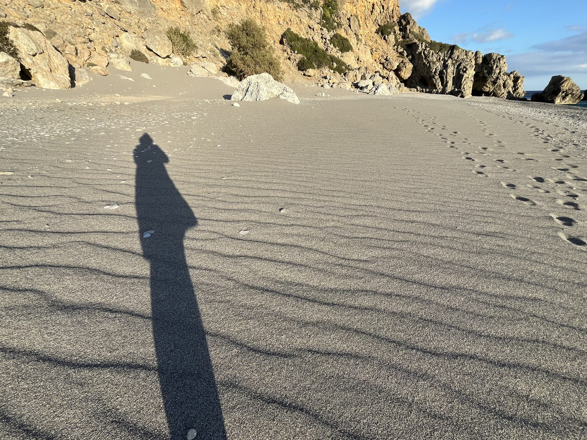 A long shadow on the dry sand below the cliffs