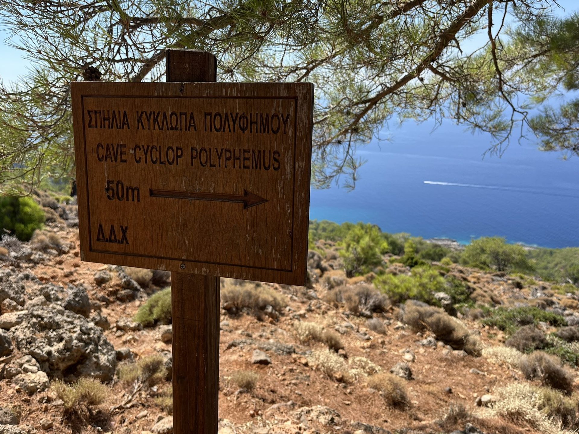 A wooden sign to the cave of the Cyclops Polyphemus, 50 metres, above the sea