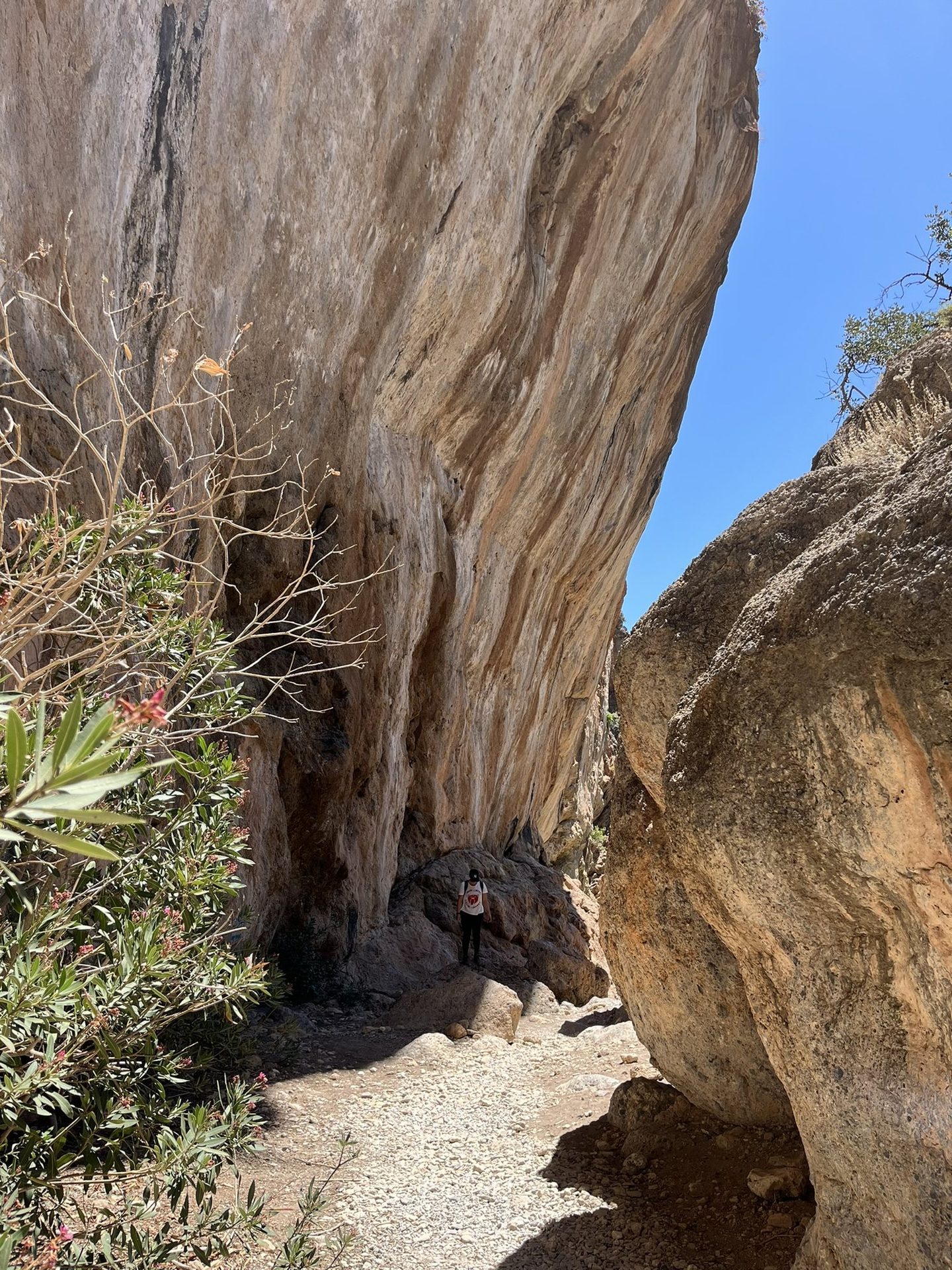 A walker under an overhanging wall of orange rock in the gorge on the path to Lissos