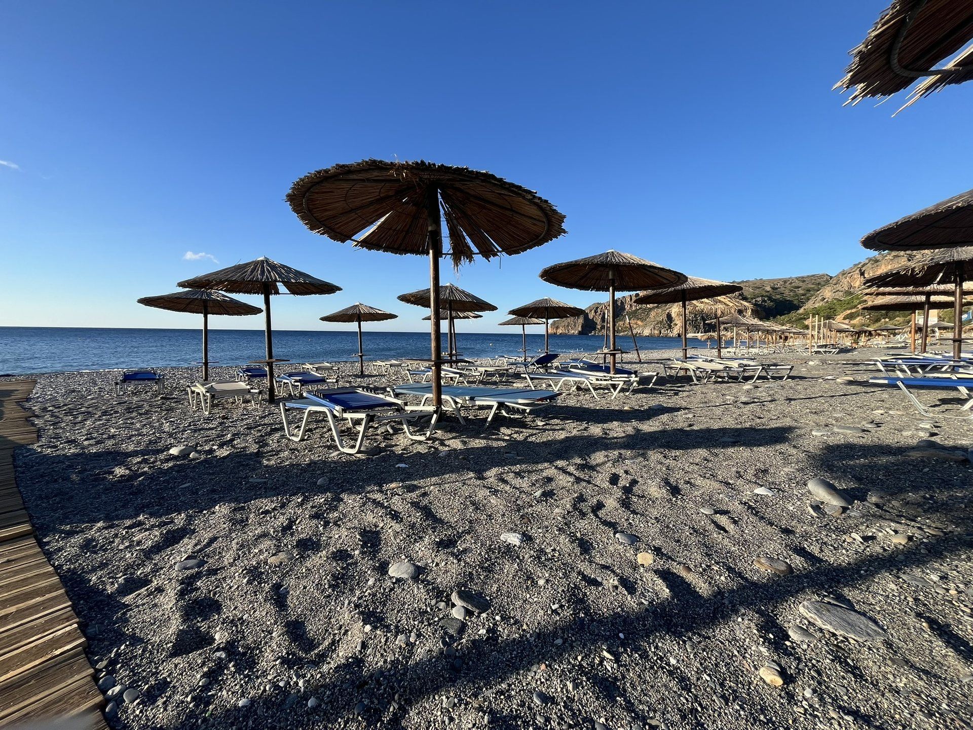 Straw umbrellas and sunbeds on the pebbles of Sougia beach, the cliffs behind
