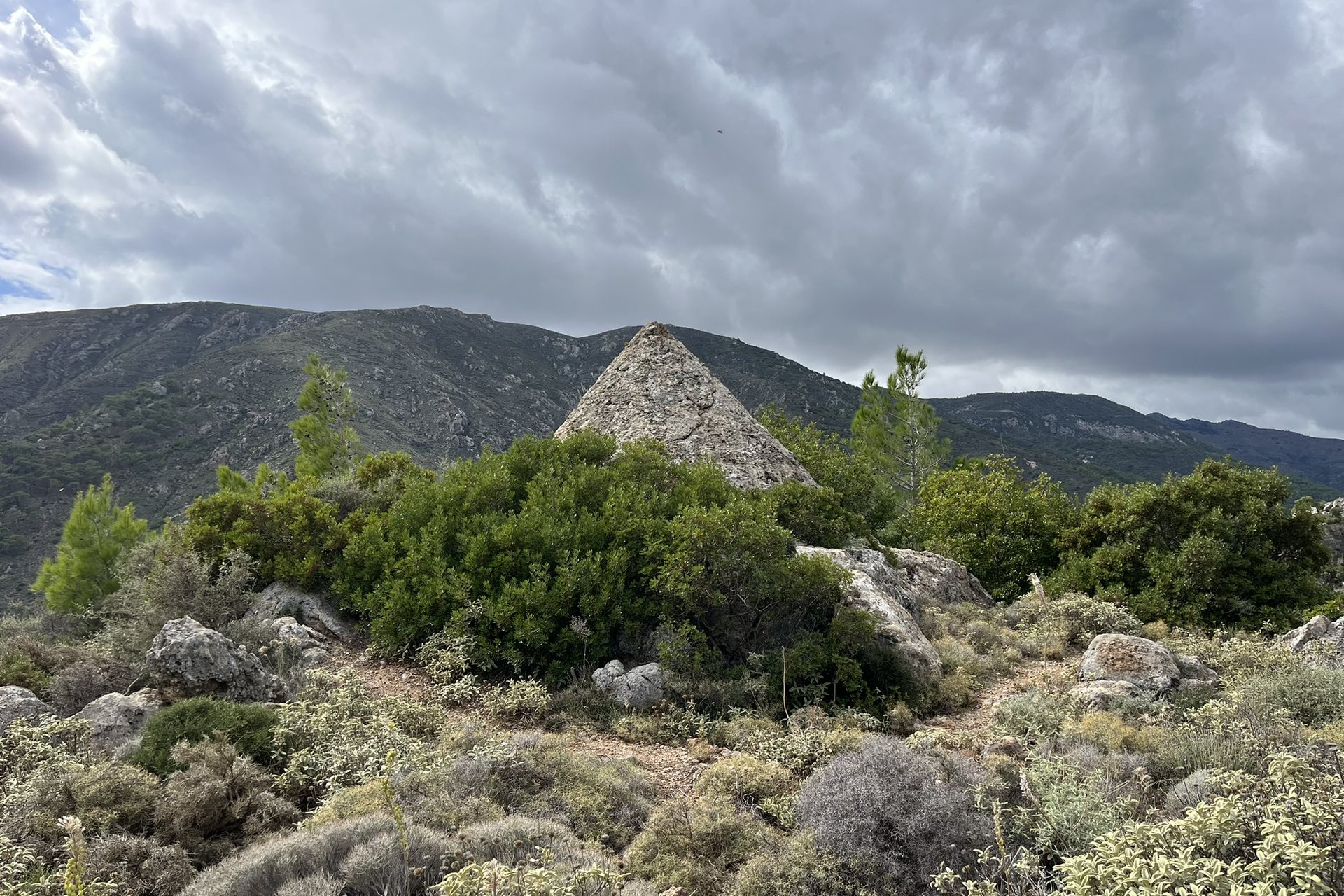 The stone cone known as the pyramid of Sougia, rising out of green scrub below the mountains