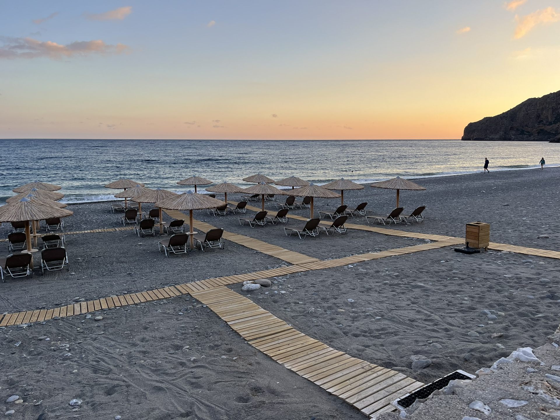 Straw umbrellas and the wooden walkway on the beach at sunset