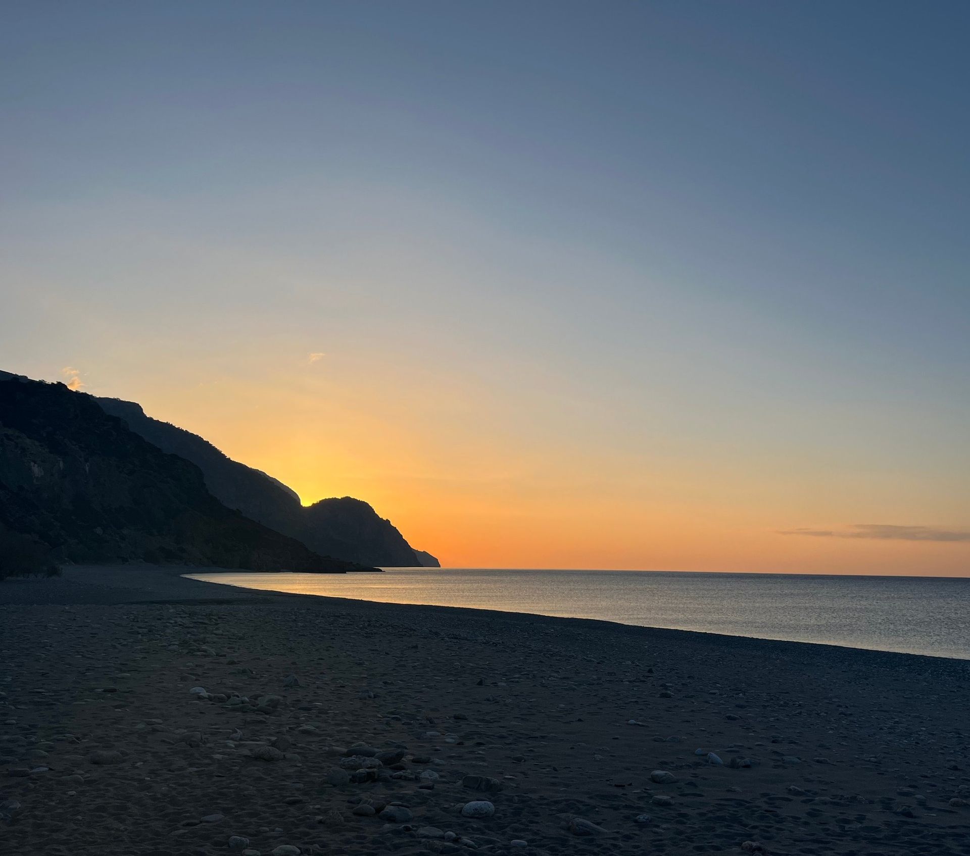 First light behind the cliffs over an empty beach